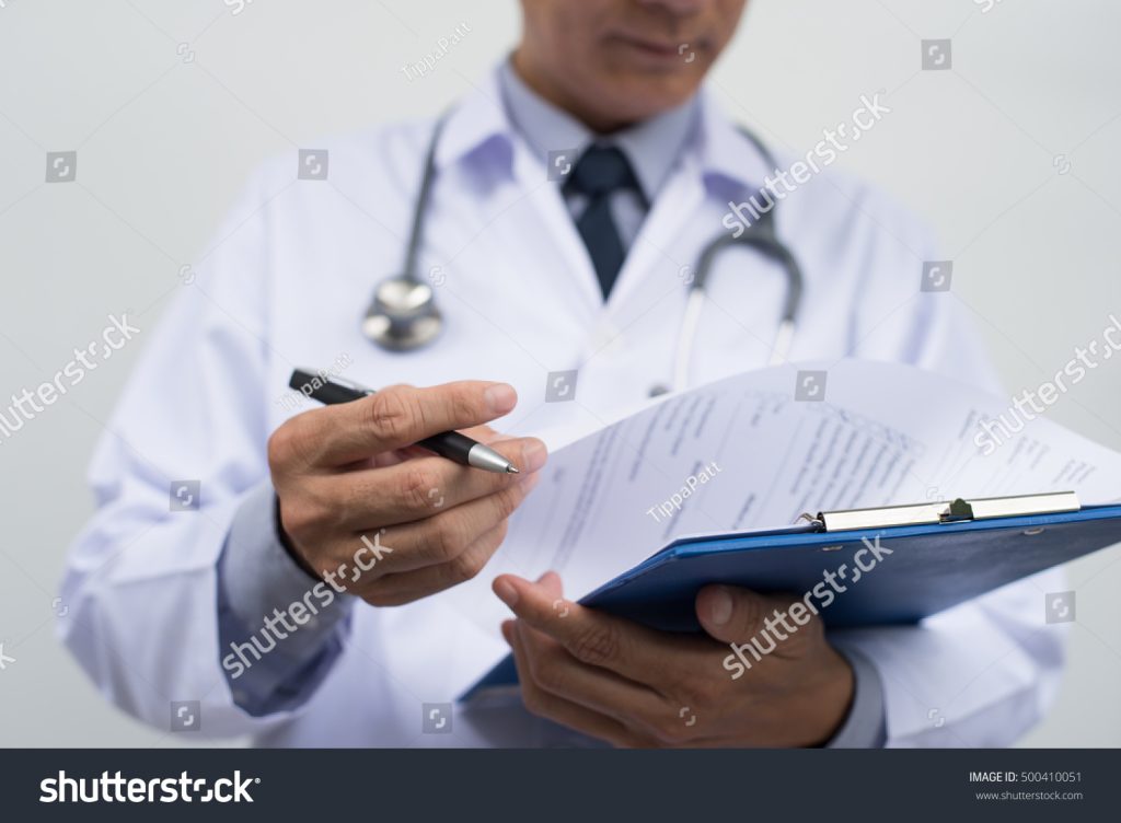 medcare vacances - stock photo male doctor on duty in white coat reading patient s information with pen in hand filling 500410051