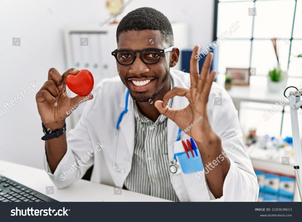 medcare vacances - stock photo young african american doctor man wearing doctor uniform holding heart at the clinic doing ok sign 2183638613
